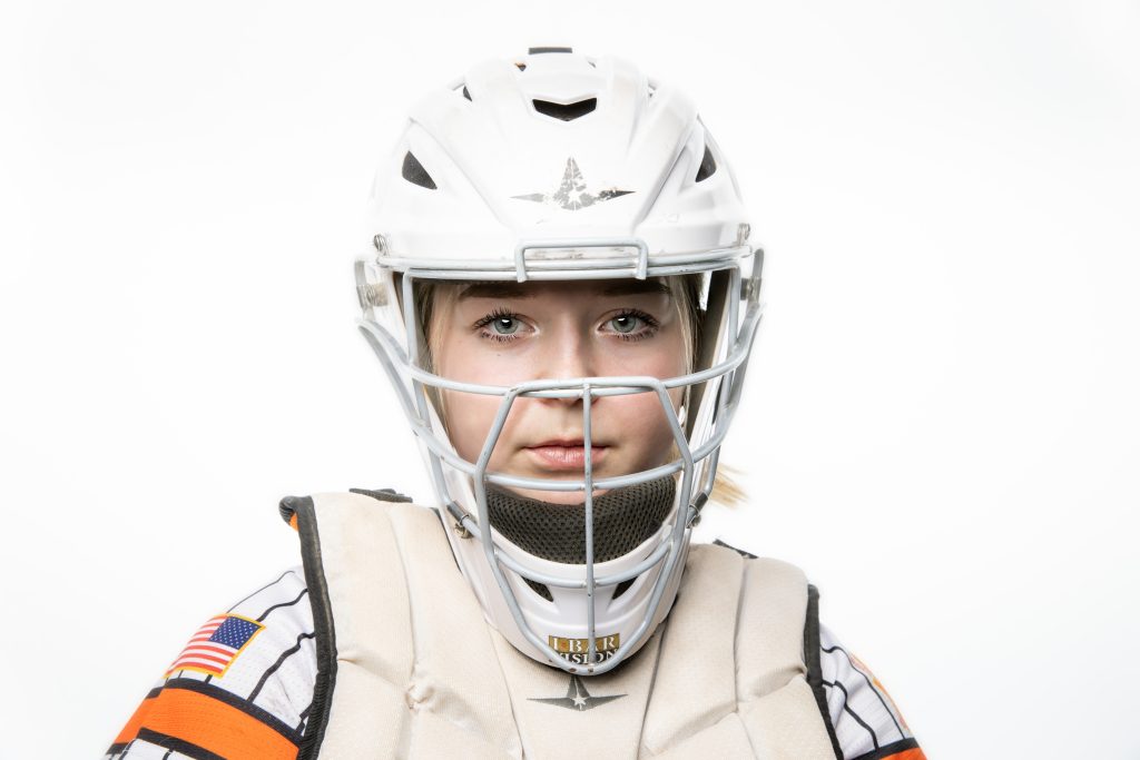 Headshot of a girls fastpitch catcher wearing a catcher's helmet.